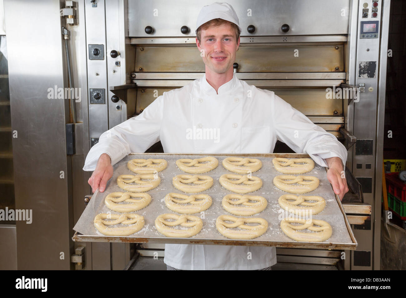 Baker in bakehouse or bakery presenting baking plate with pretzel dough Stock Photo
