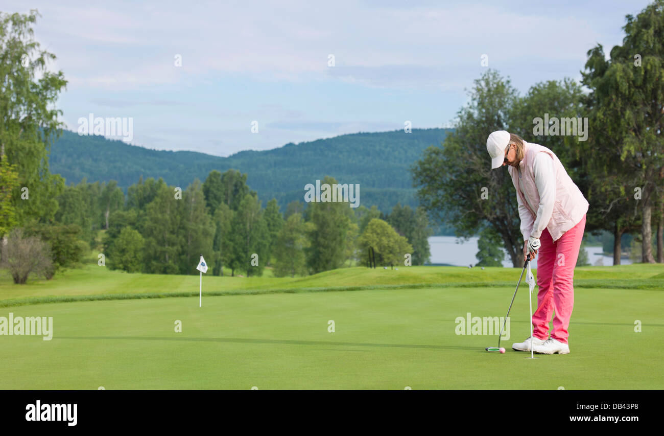 woman dressed in pink playing golf, senior citizen, green grass Stock Photo