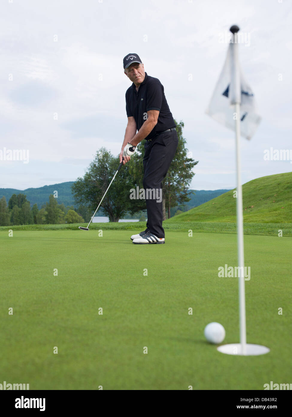 Senior citizen playing golf, dressed in black. Action shot on the puttinggreen Stock Photo