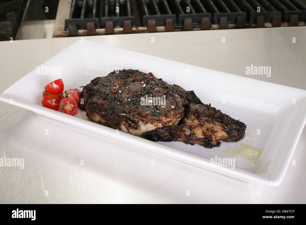 Rib-eye steak resting on the plate in the kitchen ready to serve Stock Photo