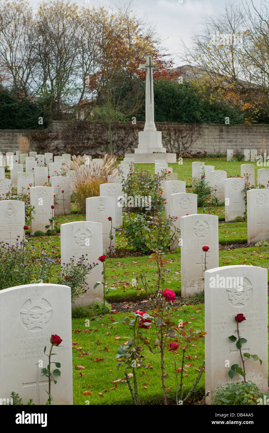 Rows of white inscribed headstones on war graves (with red rose) & Cross of Sacrifice beyond - Stonefall Cemetery, Harrogate, Yorkshire, England, UK. Stock Photo