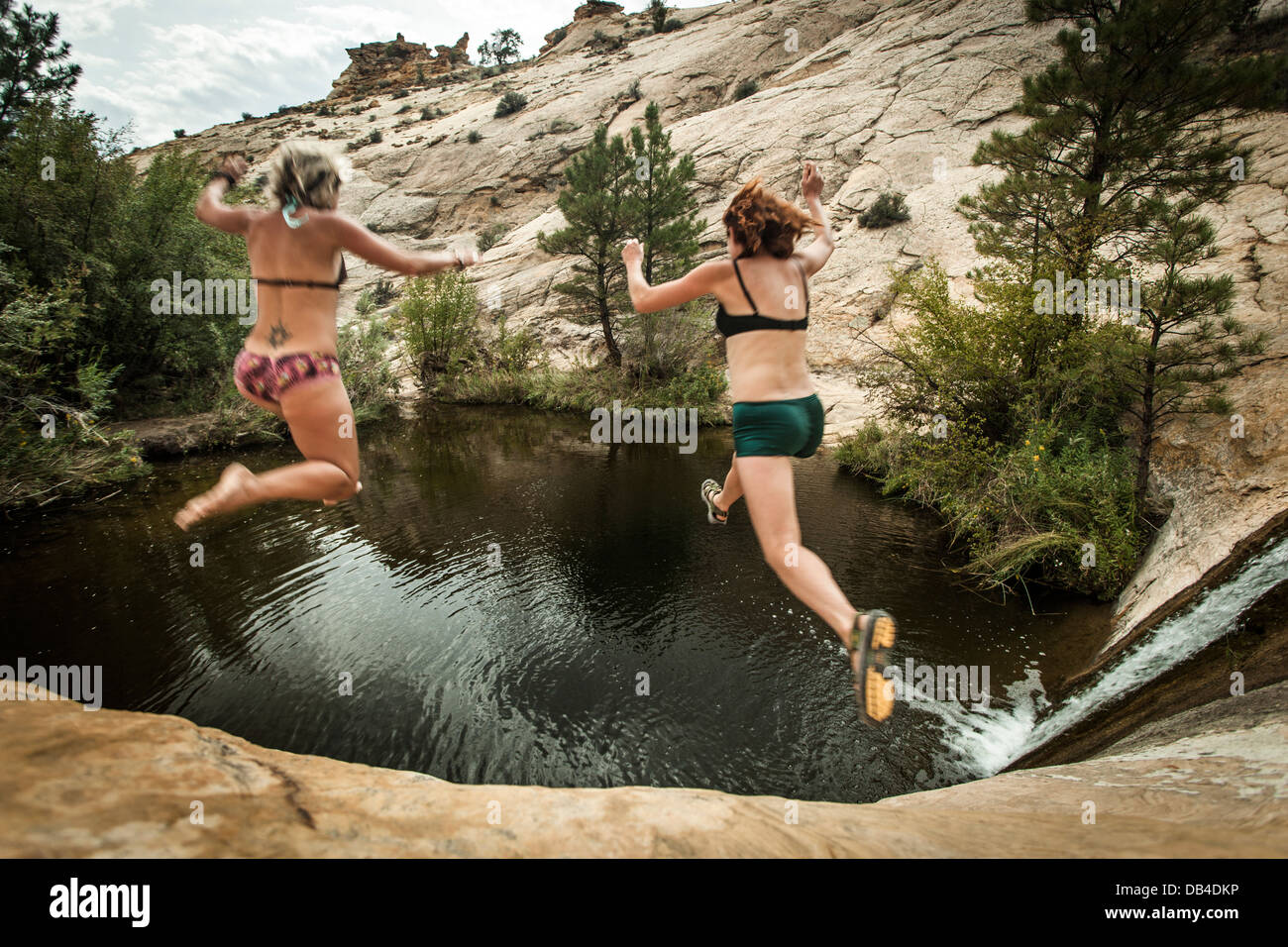 Two women jumping into a pool of water near Boulder, Utah. Stock Photo