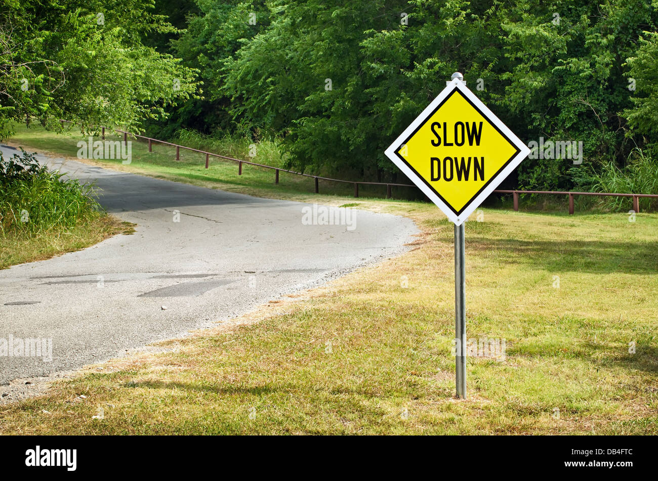 Slow Down yellow traffic sign on the roadside against green woods Stock
