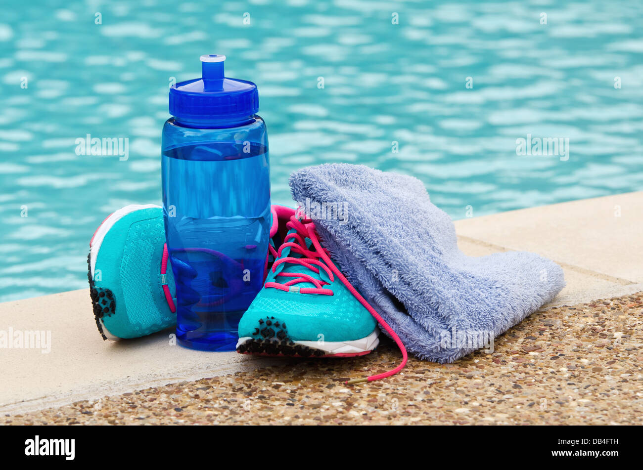 Blue water bottle with running shoes and towel by pool. Exercise and hydration concept. Stock Photo