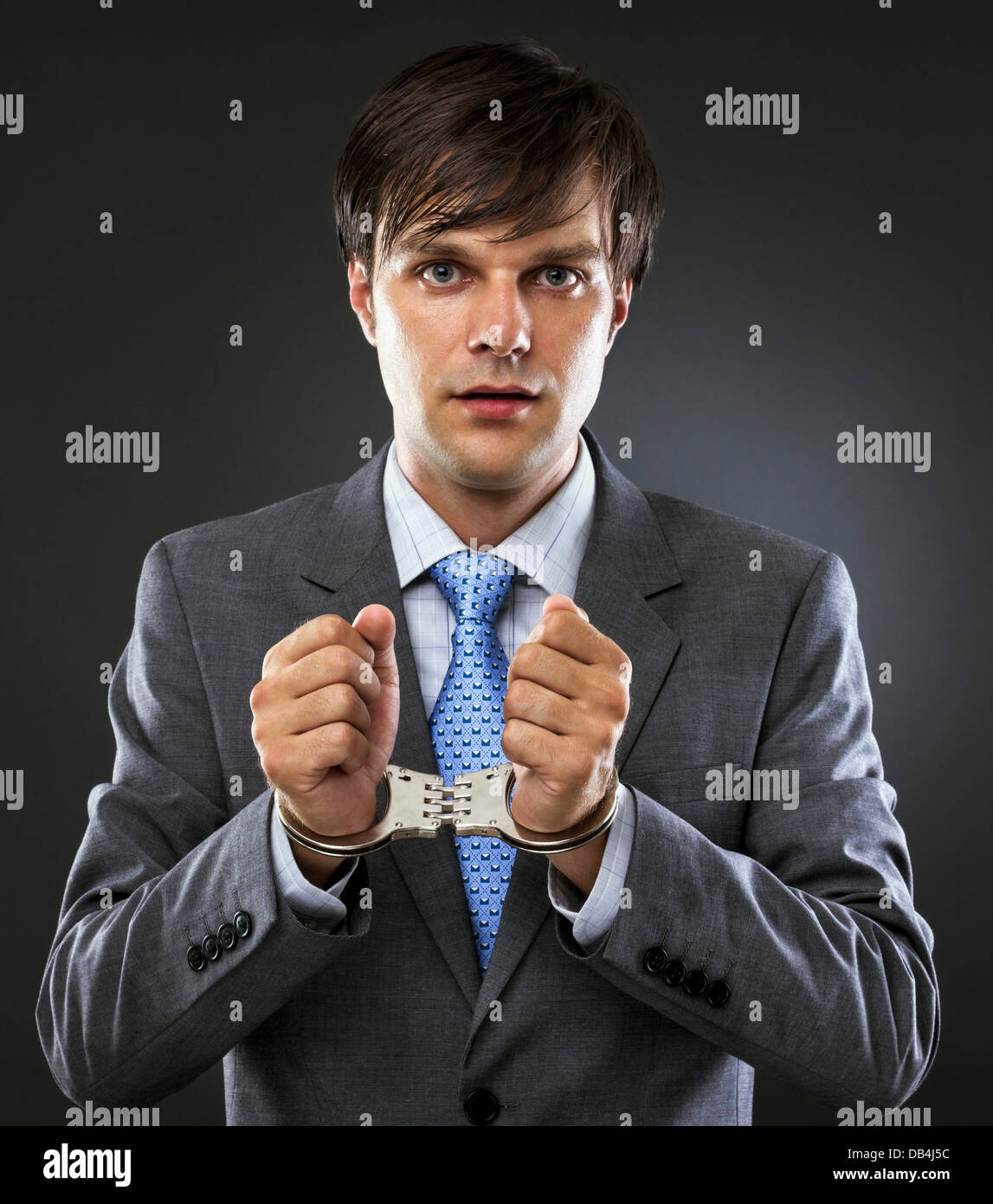 Young caucasian businessman with handcuffed hands . Studio shot. Gray