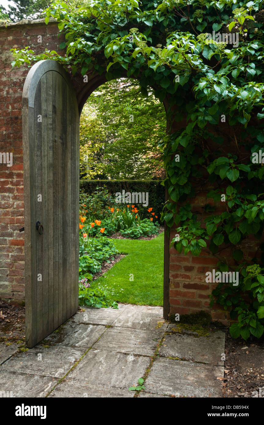 An open wooden garden door provides a 'Secret Garden' view of the Philosopher's Garden at Cottesbrooke Hall, Northamptonshire, England Stock Photo