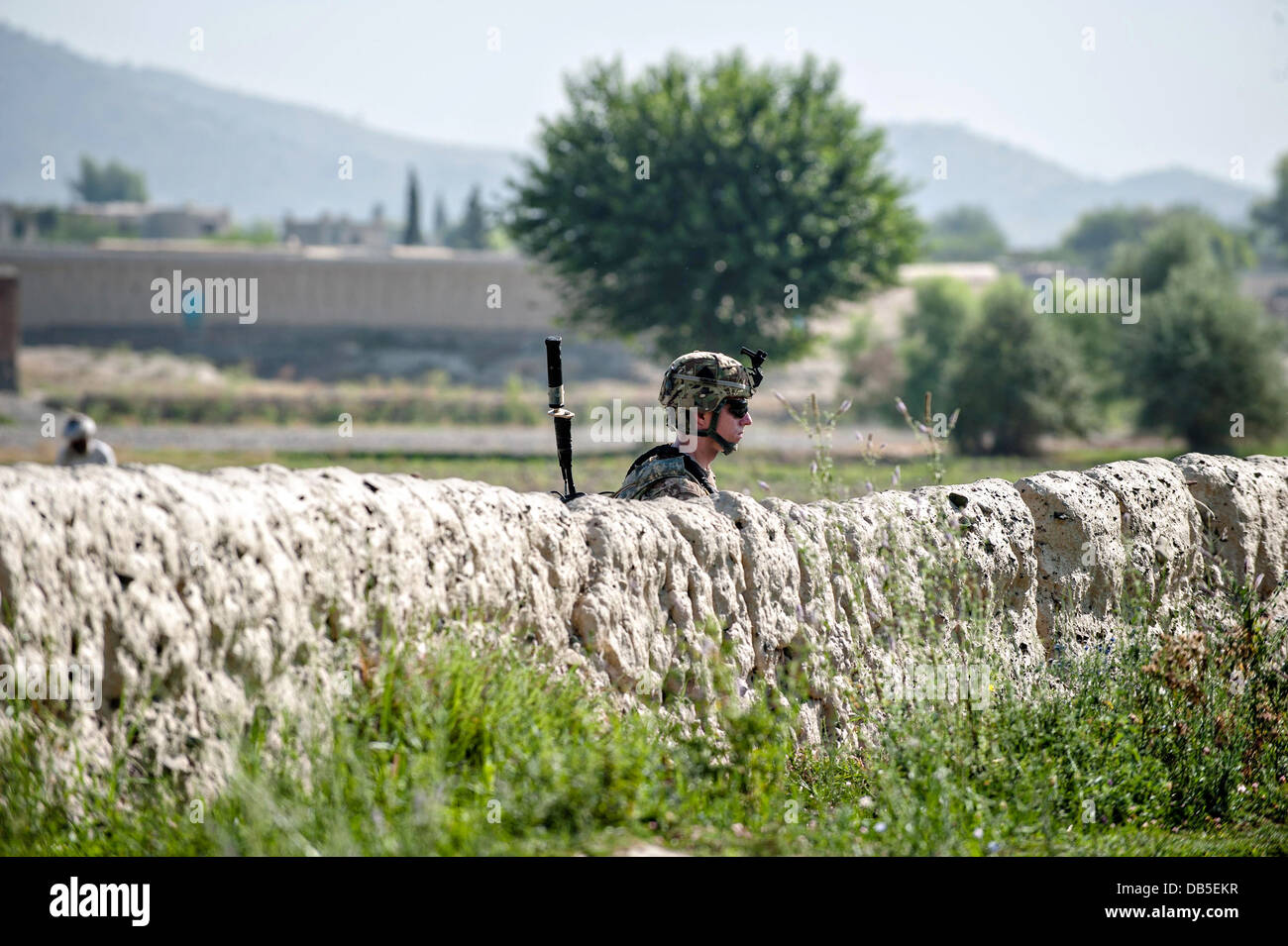 A US army soldier watches his patrol from behind a mud wall in a village near Forward Operating Base Salerno July 4, 2013 in Khost province, Afghanistan. Stock Photo