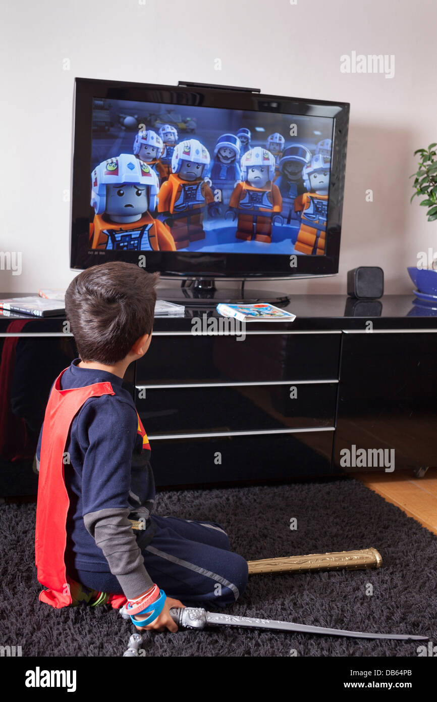 Child wearing a superhero costume watches television Stock Photo