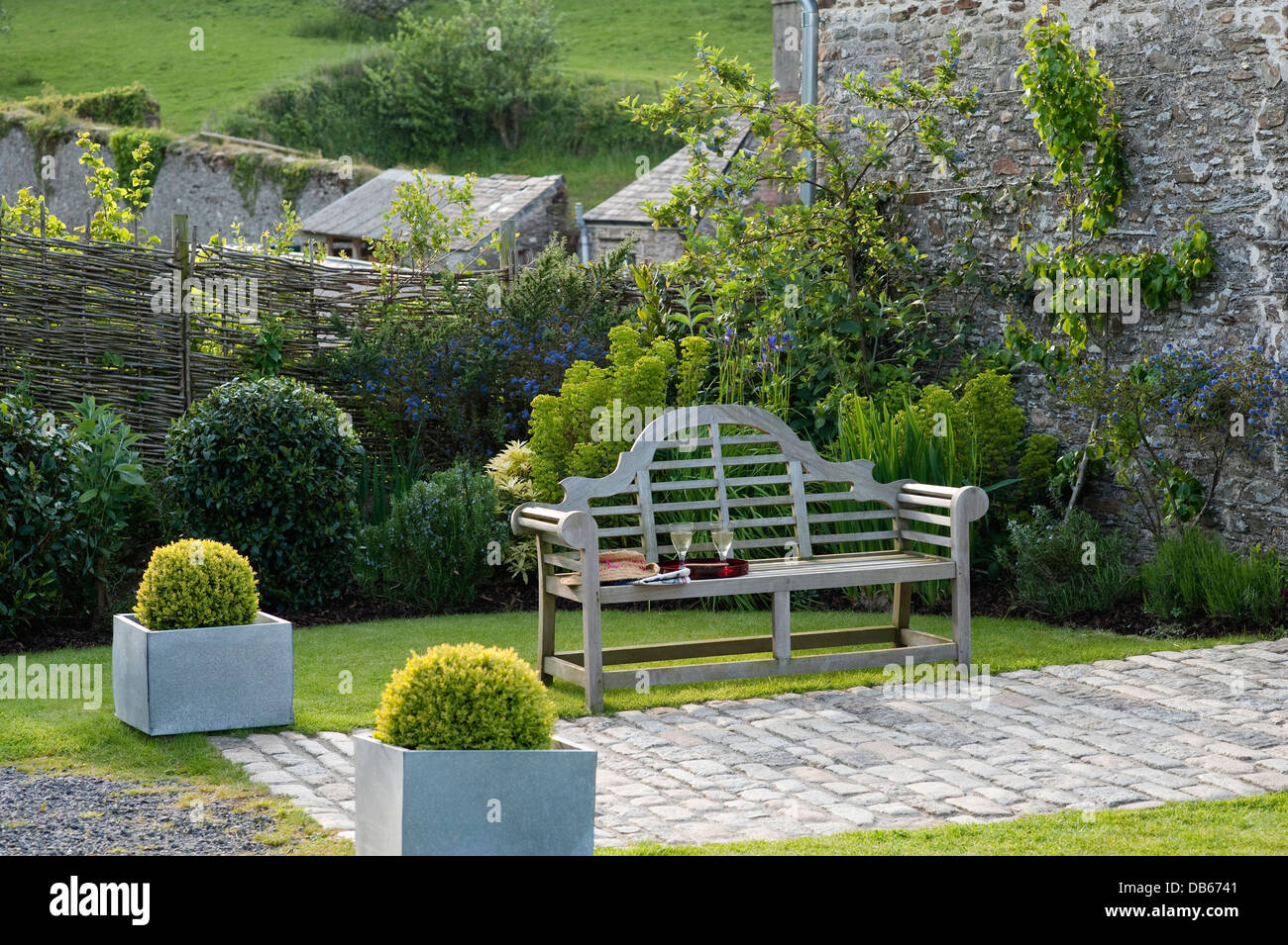Glasses and tray rest on bench in garden of 18th century farmhouse, Devon Stock Photo