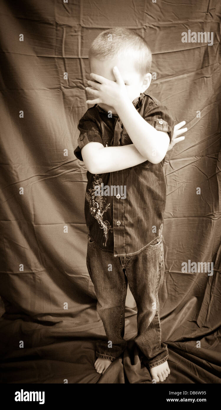 A six year old boy with autism hides his face from the camera with his