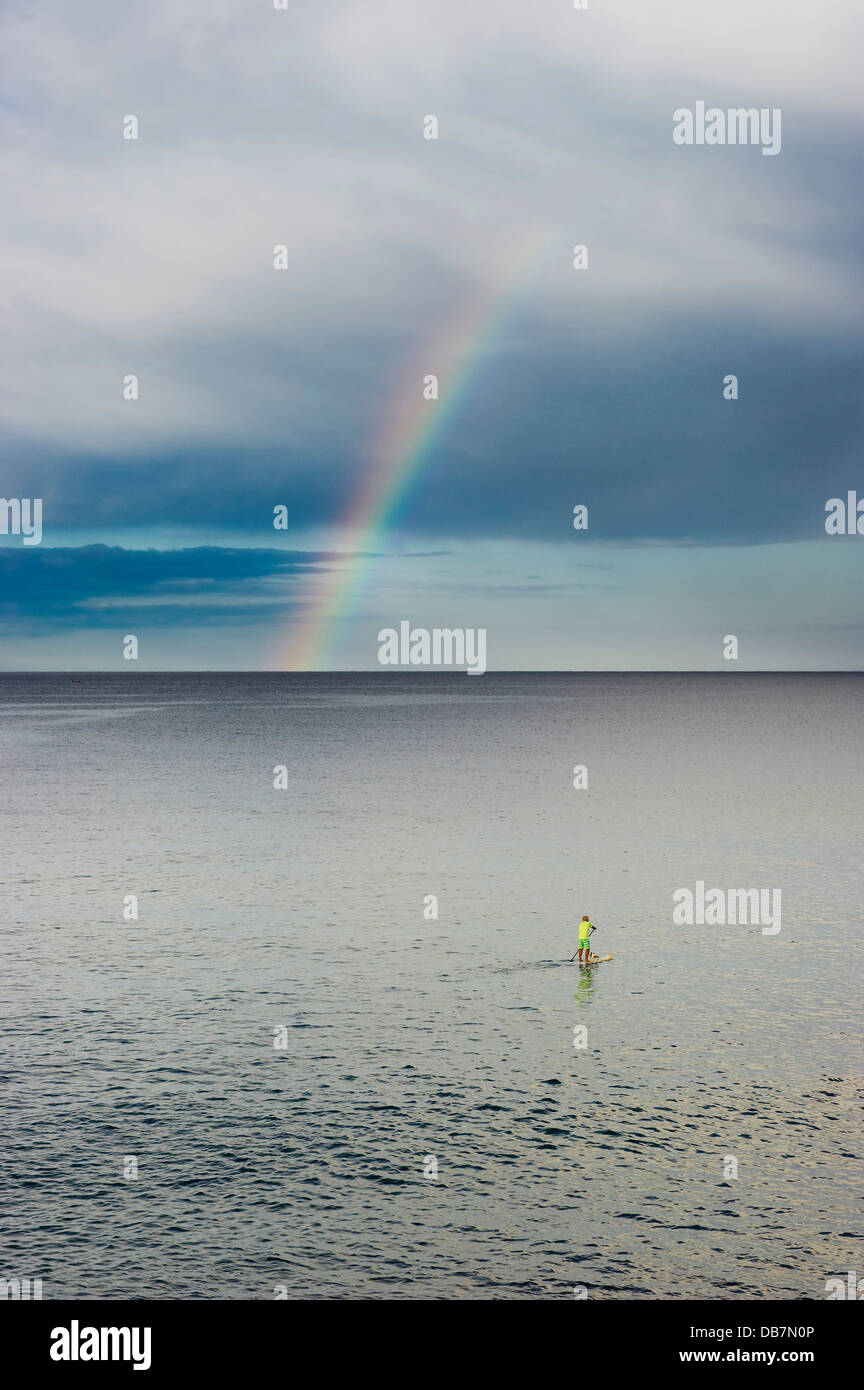 Stand up paddler with rainbow over the sea Stock Photo