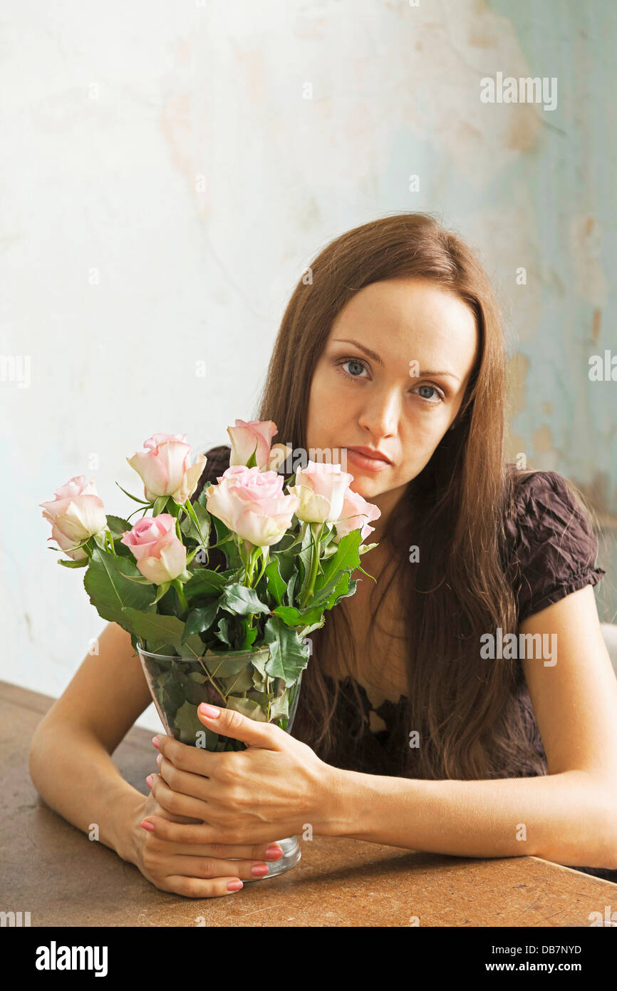 Young woman sitting at a table with flowers in a vase Stock Photo - Alamy