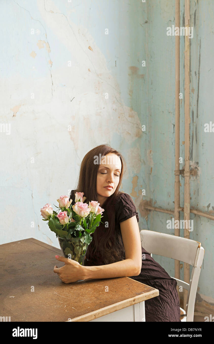 Young woman sitting at a table with flowers in a vase Stock Photo - Alamy