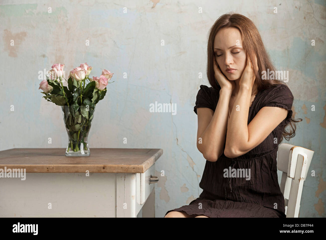 Young woman sitting at a table with flowers in a vase Stock Photo - Alamy