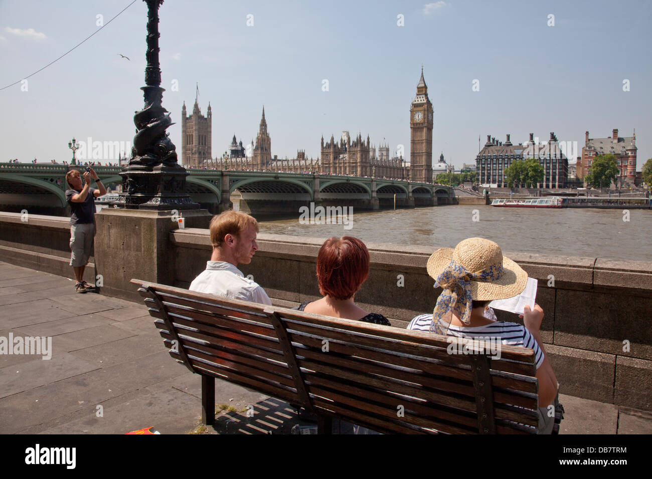 Tourists sit on bench opposite Houses of Parliament by Thames river in London Stock Photo