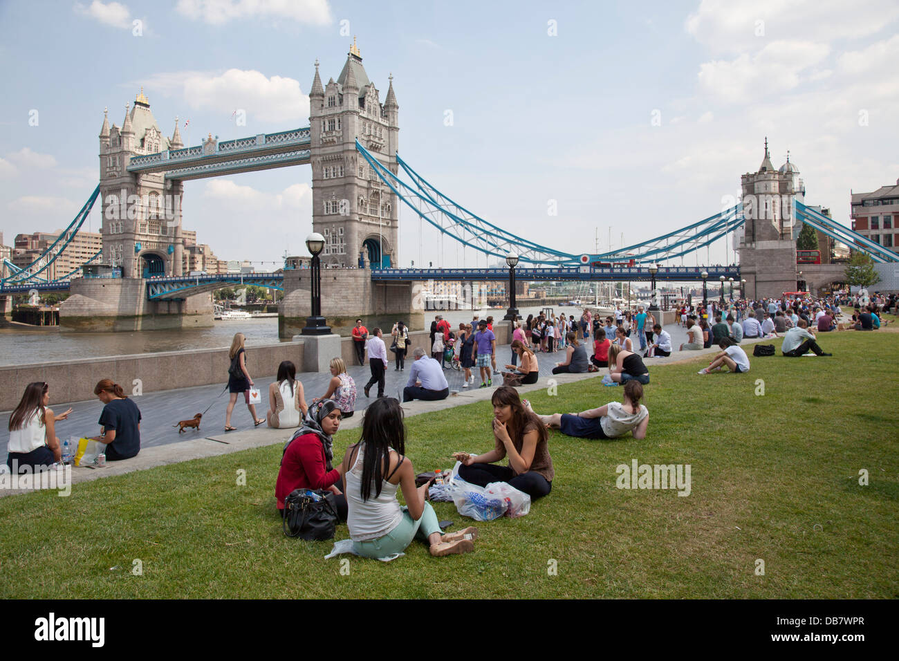 People relaxing on the park by Thames river and Tower Bridge, London