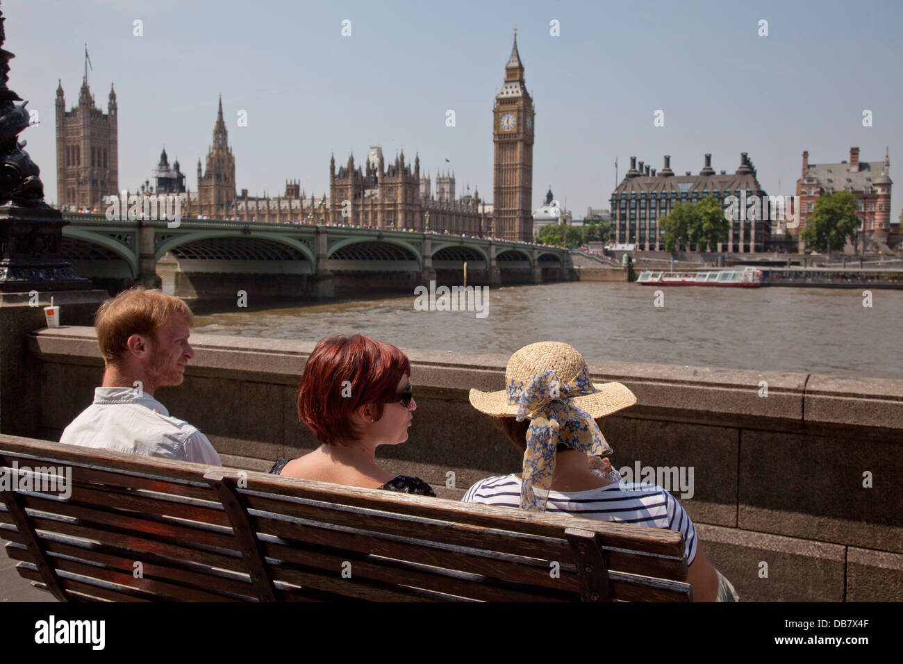 Tourists sit on bench opposite Houses of Parliament by Thames river in London Stock Photo