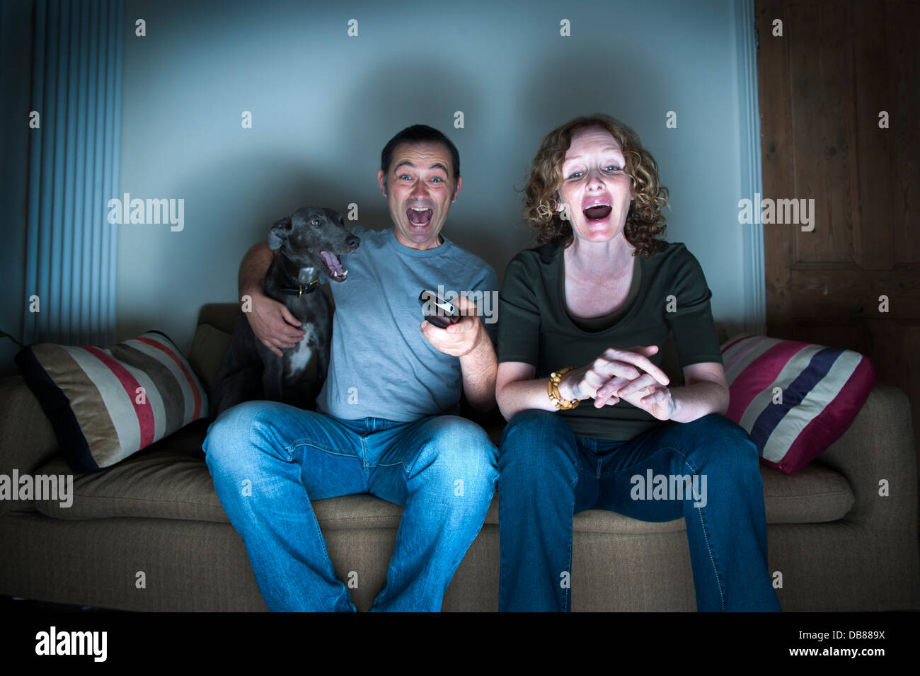 middle aged couple and dog watching the television laughing Stock Photo