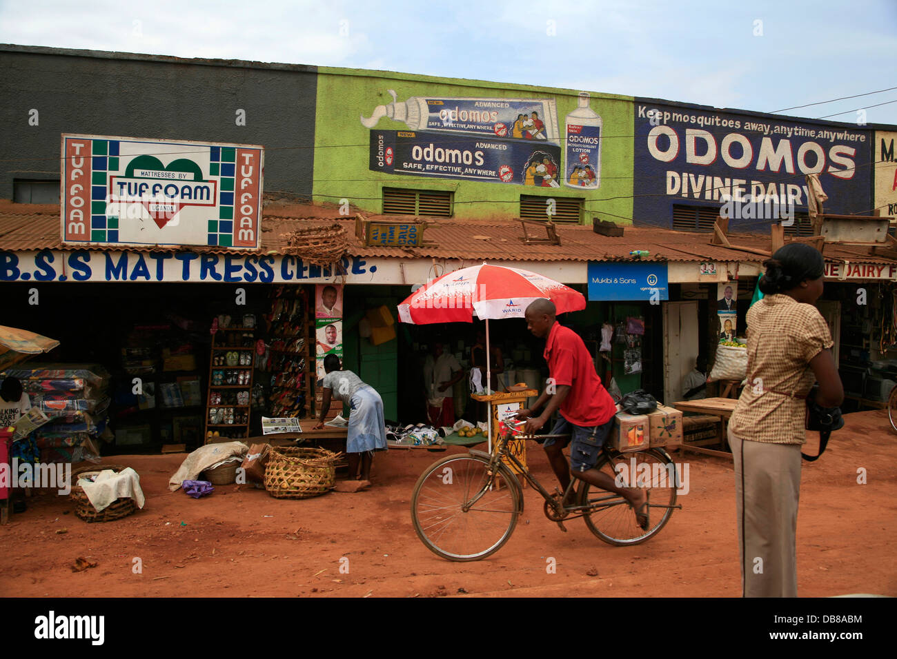 African man rides a bicycle past small shops, Uganda Stock Photo
