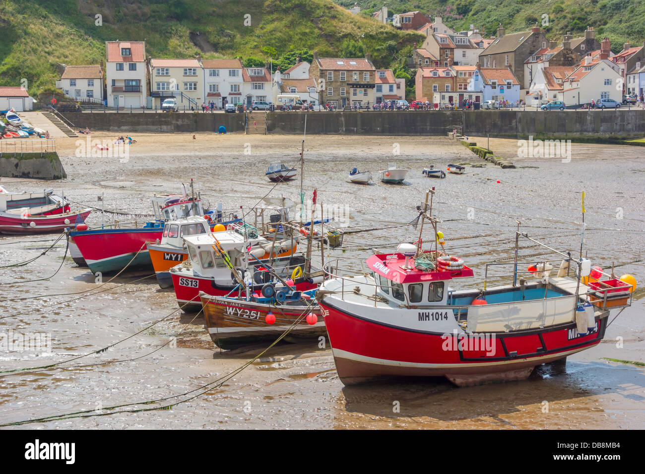 A line of fishing boats lie on the sand at low tide in Staithes Harbour ...