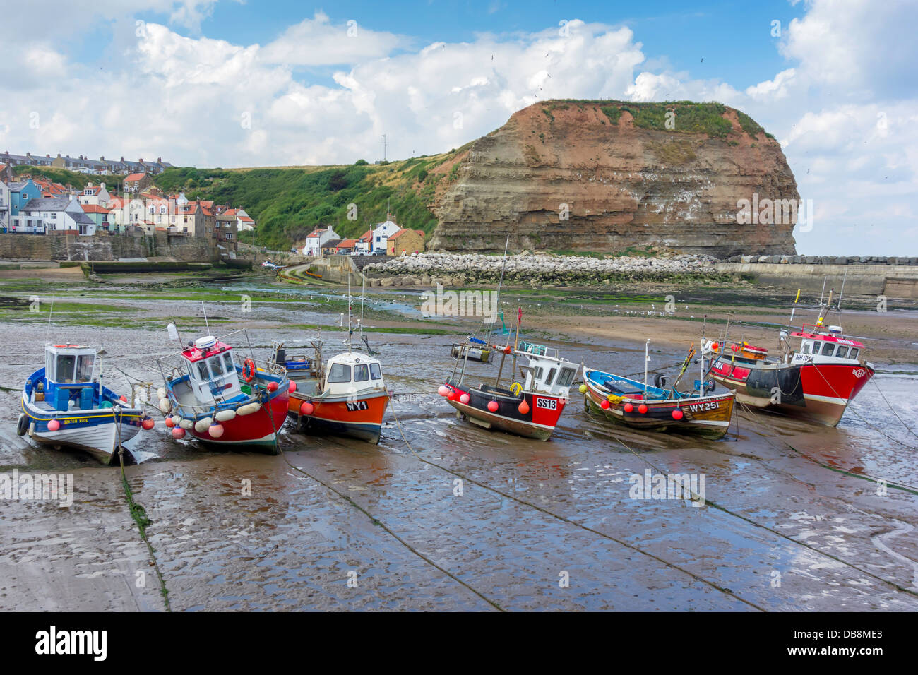 A line of fishing boats lie on the sand at low tide in Staithes Harbour ...