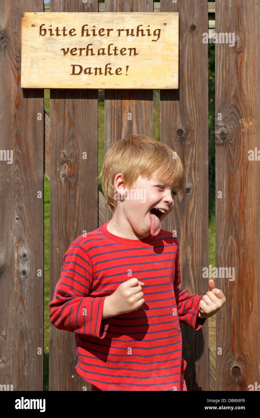 young boy screaming in front of a sign asking for silence Stock Photo