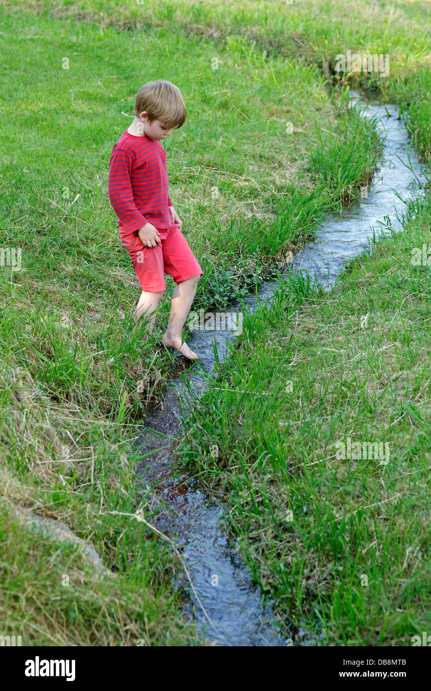young boy playing beside a stream Stock Photo