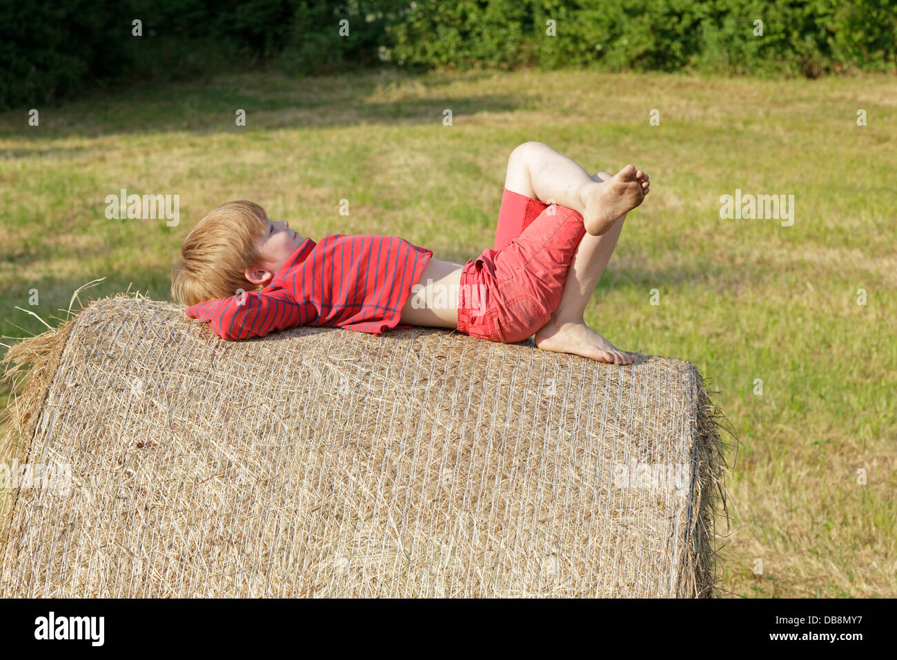 young boy resting on a bale of hay Stock Photo
