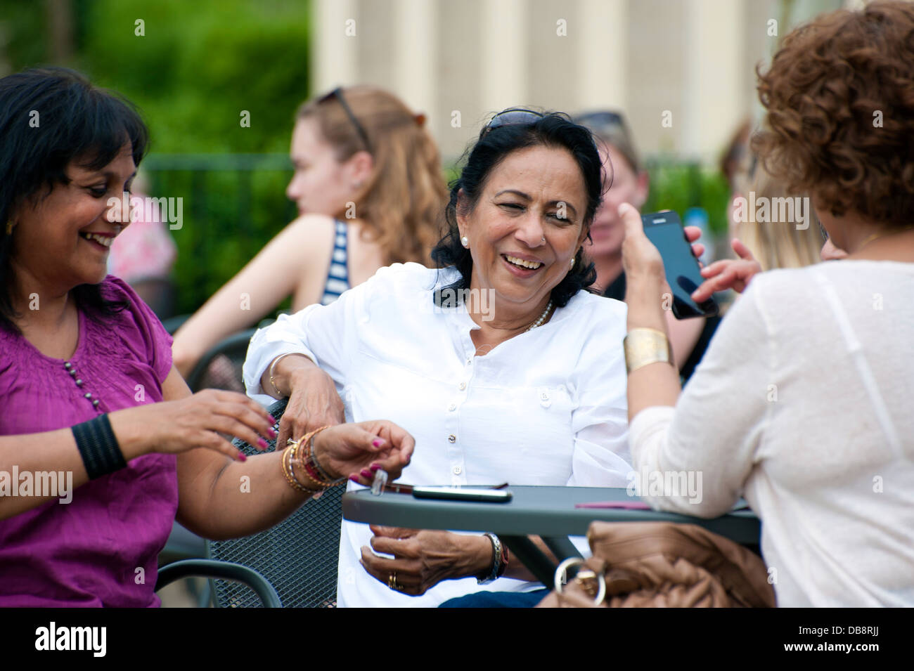 three mature woman meeting up laughing one on mobile phone mobile phones on table. outdoor garden Stock Photo