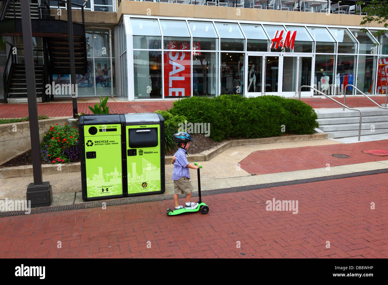 Boy riding scooter past BigBelly solar powered, rubbish-compacting and recycling bins, Inner Harbor, Baltimore , Maryland, USA Stock Photo
