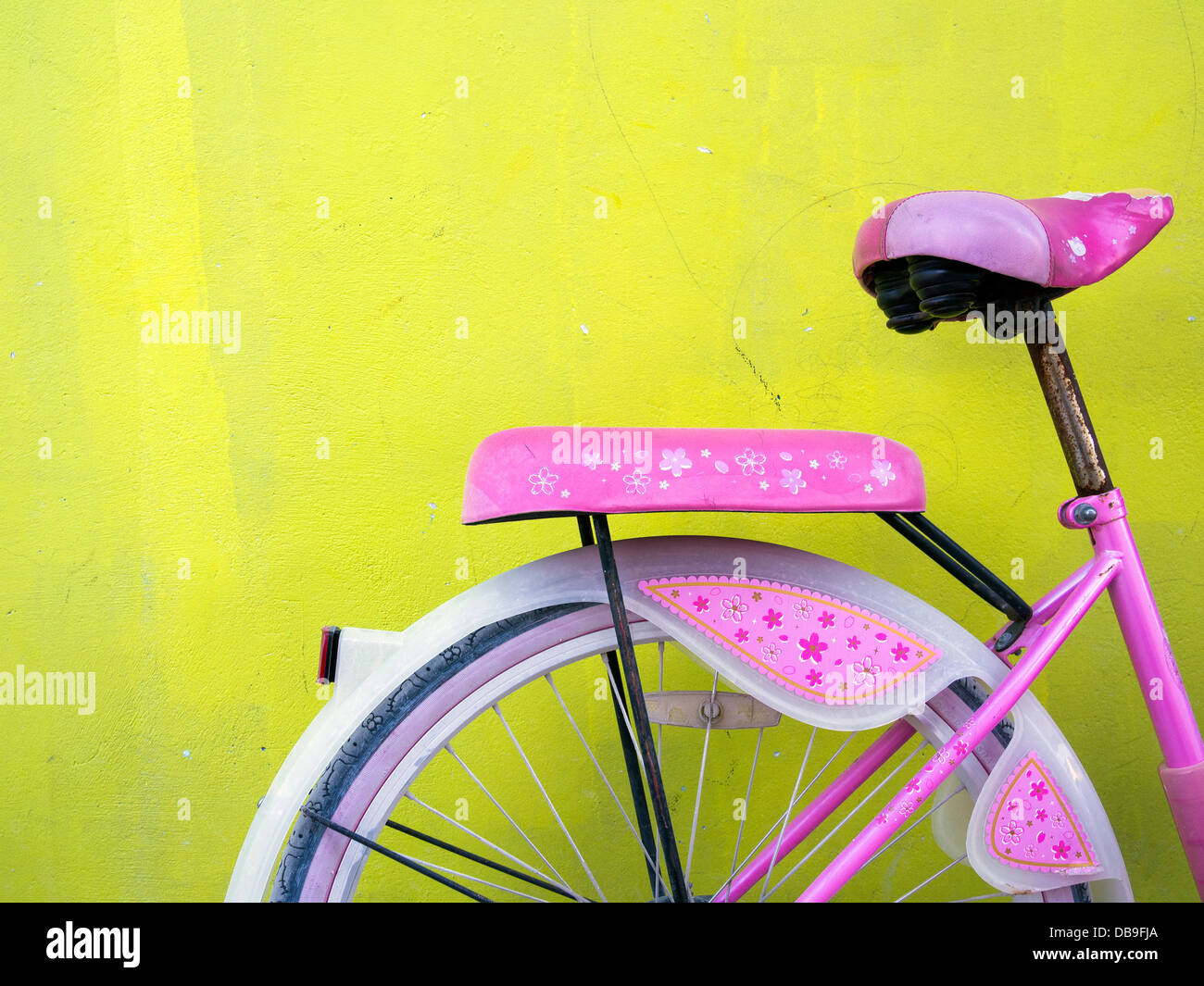 Pink girl's bike with mudguards against a yellow wall Stock Photo