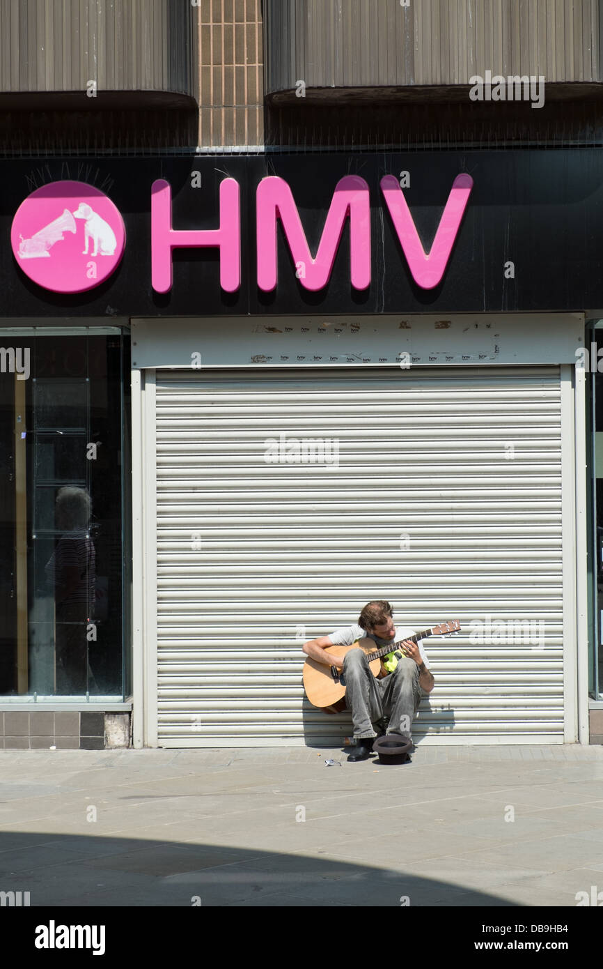 A busker busking, playing guitar & singing outside of a closed store of the troubled group HMV Stock Photo