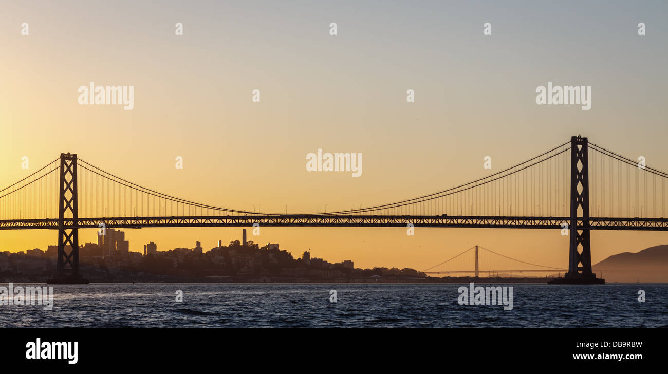 Panoramic view of San Francisco's Bay Bridge and Golden Gate Bridge at sunset with blue, orange and golden sky Stock Photo