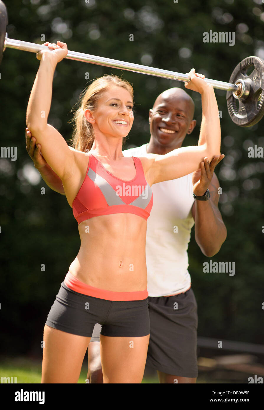Woman with personal trainer lifting weights during outdoor exercise programme Stock Photo