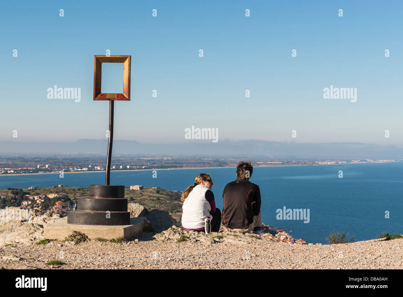 A couple sitting next to one of Marc Andre de Figueres's scuplture, taking and enjoying the coastal view, near Collioure, France Stock Photo