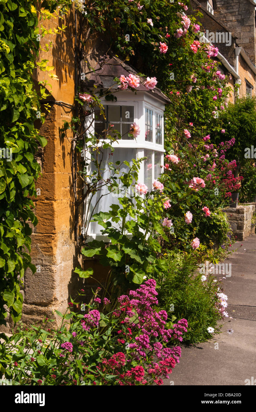 Colourful roses and summer flowers grow around a stone cottage in the