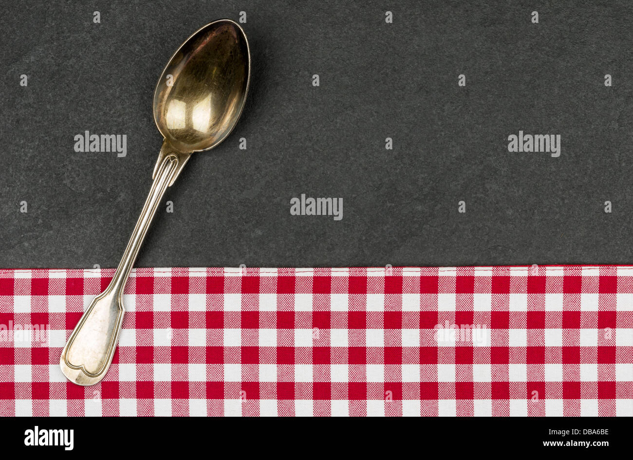 Silver spoon on a slate plate with a red checkered tablecloth Stock Photo