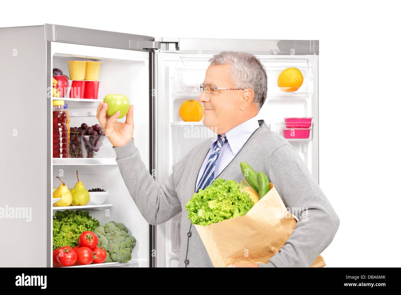 Smiling mature man holding a paper bag near the refrigerator full of healthy products Stock Photo