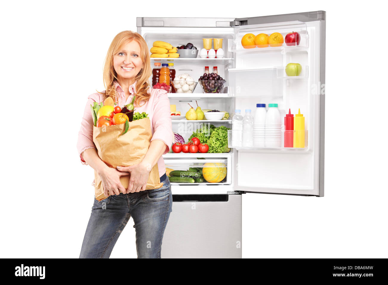 Smiling mature woman holding a paper bag full of groceries in front of refrigerator Stock Photo