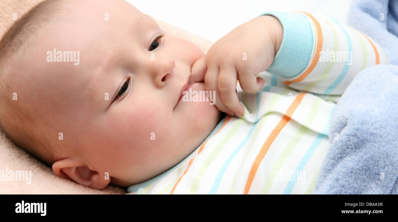 baby in bed with finger in mouth Stock Photo