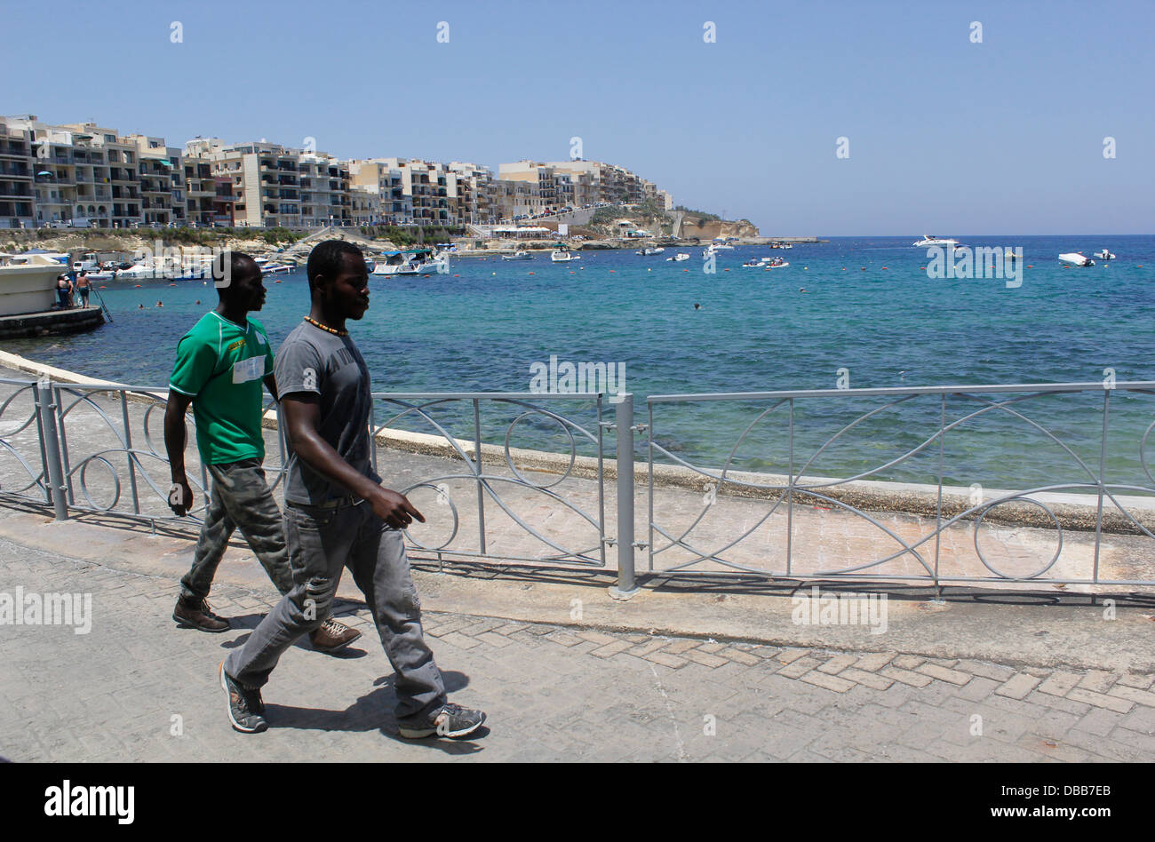 African migrants walk along the seacoast of the village of Marsalforn in the island of Gozo the sister island of Malta Stock Photo