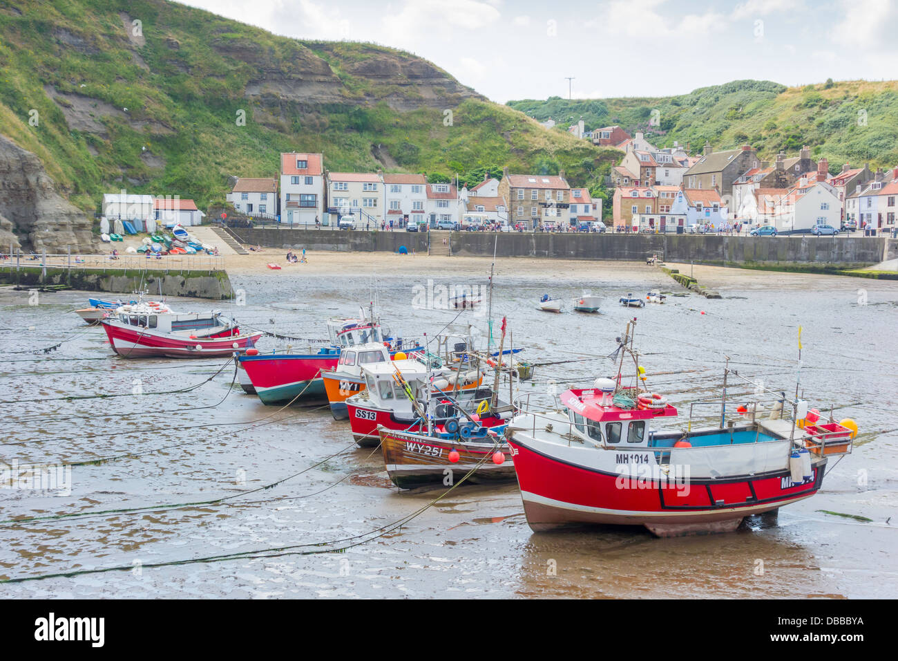 A line of fishing boats lie on the sand at low tide in Staithes Harbour ...