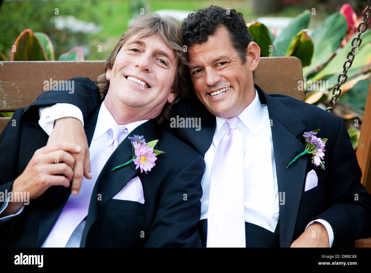 Handsome gay couple relaxing on a swing at their wedding reception.  Stock Photo