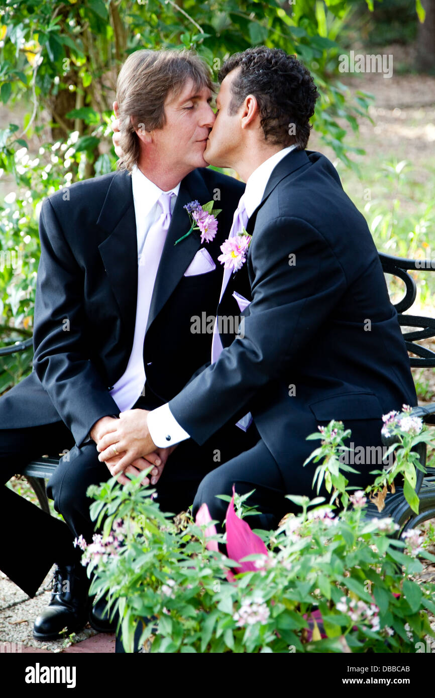 Handsome gay wedding couple kissing outdoors in the garden on their wedding day.  Stock Photo