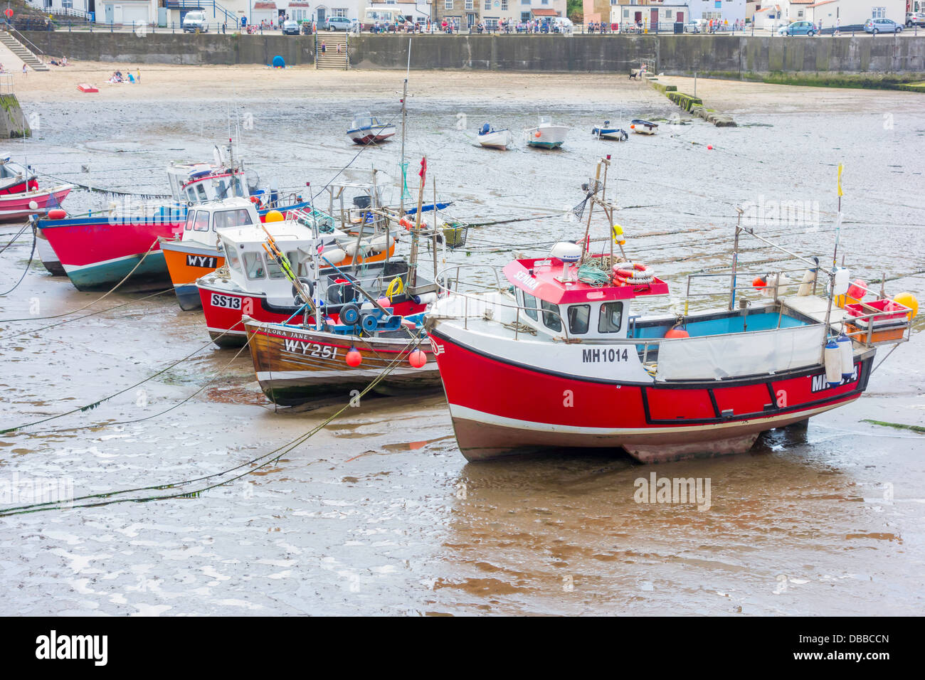 A line of fishing boats lie on the sand at low tide in Staithes Harbour ...