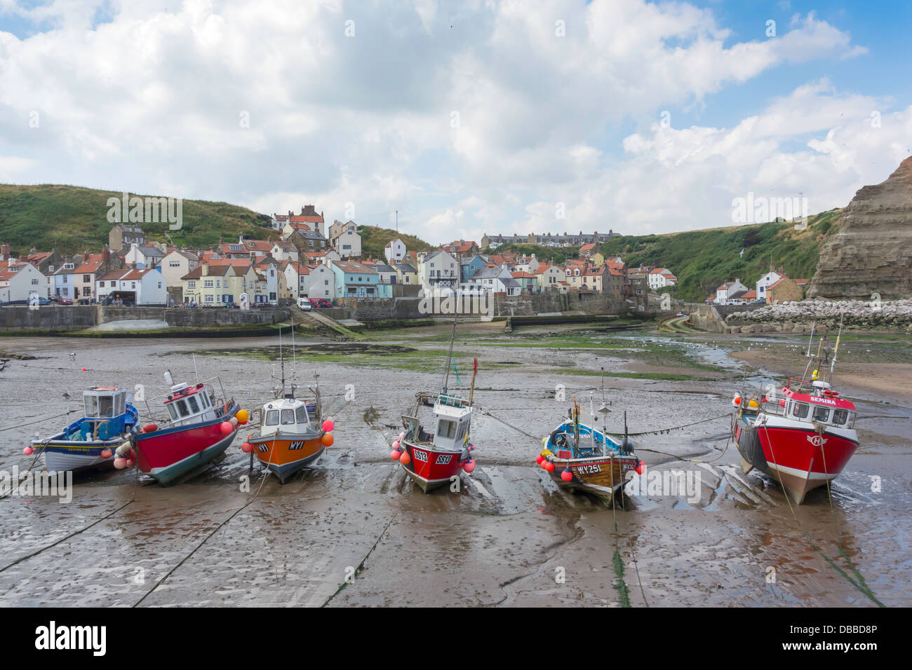 A line of fishing boats lie on the sand at low tide in Staithes Harbour ...