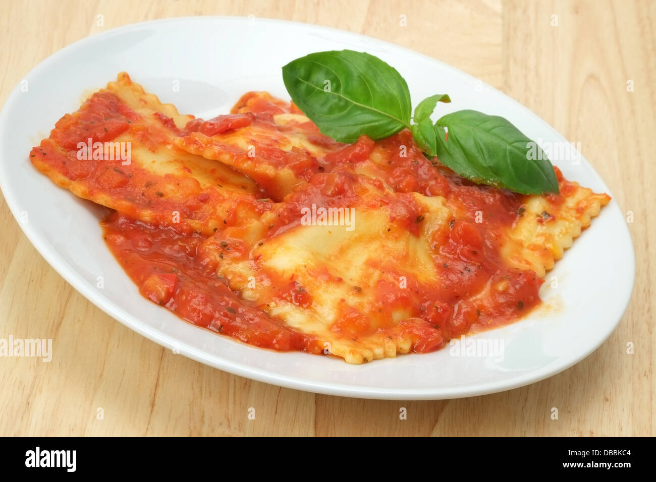 Cheese filled ravioli pasta in a red tomato sauce with a basil leaf garnish. Stock Photo