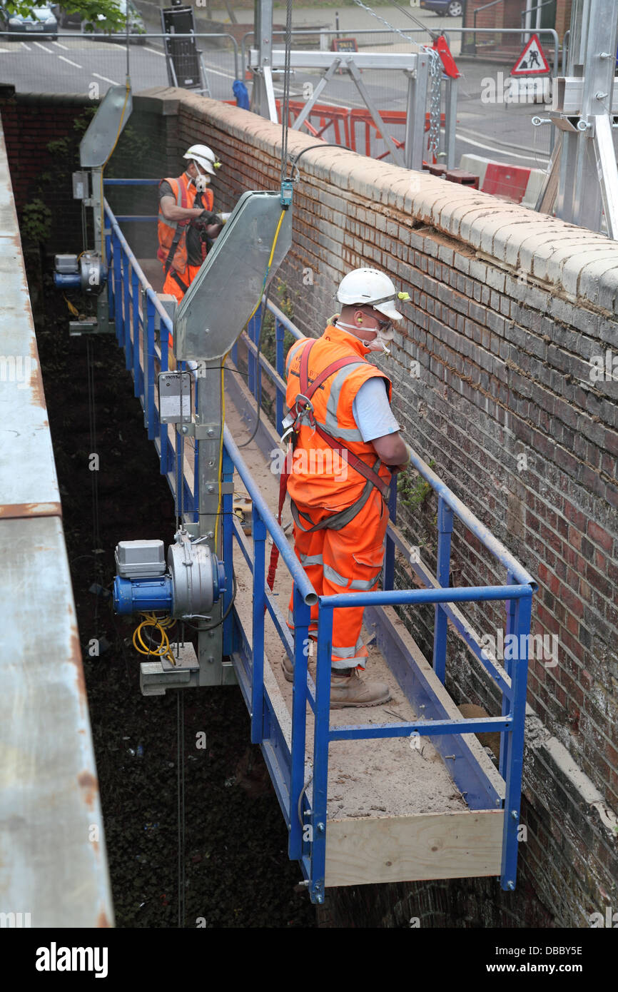 Workmen renovate the brick parapet to a road bridge over a railway ...