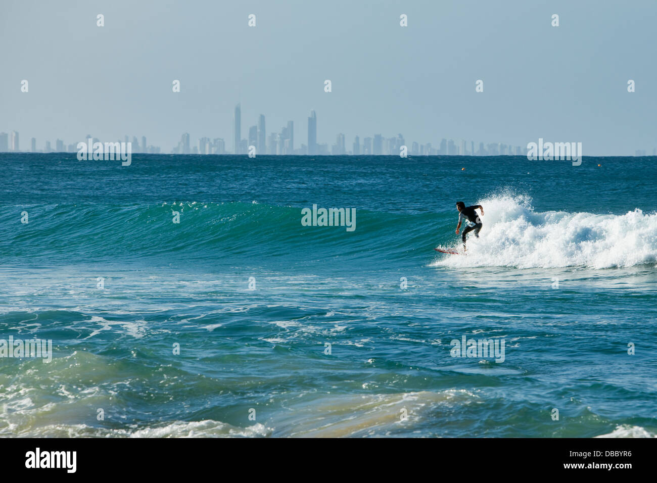 Surfer riding a wave with Surfers Paradise skyline in background. Rainbow Bay, Coolangatta, Gold Coast, Queensland, Australia Stock Photo