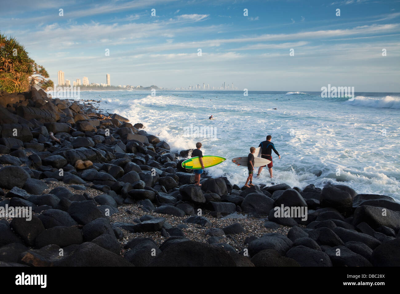 Surfers climbing over rocks to reach surf at Burleigh Heads. Gold Coast